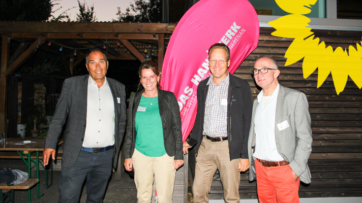 Foto von Vertretern der Handwerkskammer und der Grünen vor pinker Flagge der Handwerkskammer in Abendstimmung